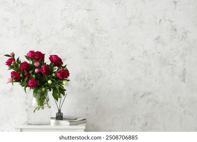 Vase with peonies, magazines and aroma sticks on coffee table near beige grunge wall - Powered by Shutterstock