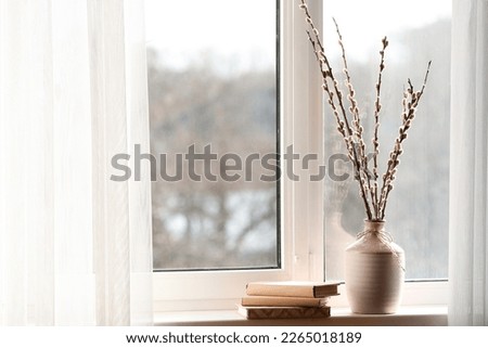 Vase with pussy willow branches and books on windowsill in room