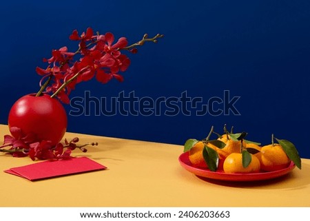 A vase of red orchids, a plate of tangerines and red envelopes are displayed on a blue and yellow background. Empty space for product display.
