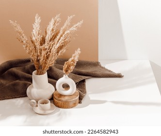 Vase set with pampas grass and ceramic candle with brown towel at the background. Cozy home decorations with warm sunlight and shadows, copy space. Bohemian style