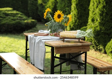 Vase with sunflowers, grapes, pie and corncobs on wooden table in garden - Powered by Shutterstock