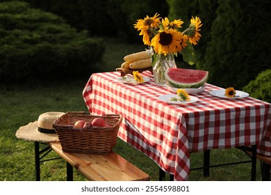 Vase of sunflowers, watermelon, corn and plates on table in garden - Powered by Shutterstock