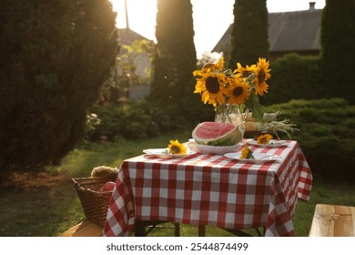 Vase of sunflowers, watermelon and plates on table in garden - Powered by Shutterstock