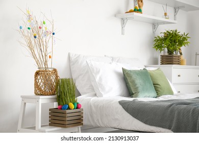 Vase with tree branches and Easter eggs in box on stepladder near light wall in bedroom