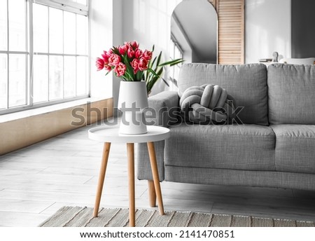 Vase with tulip flowers on small table and sofa in living room