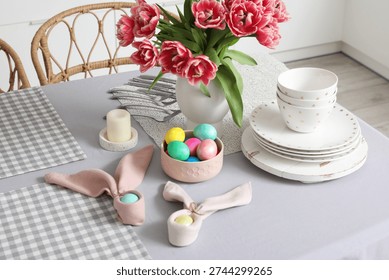 Vase with tulips, Easter eggs and dinnerware on dining table in kitchen