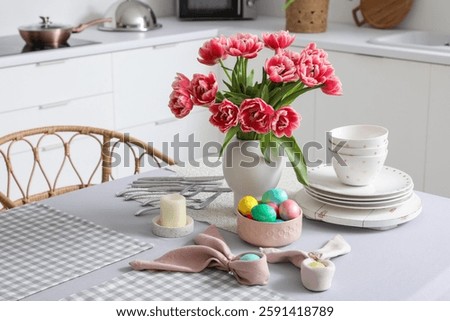 Vase with tulips, Easter eggs and dinnerware on dining table in kitchen