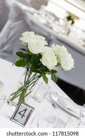 A vase of white roses in and crystal wine glasses.