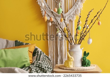 Vase with willow branches, Easter eggs and rabbits on table in living room