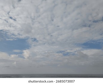 A vast, cloudy sky with hints of blue peeking through, above a calm, dark body of water.