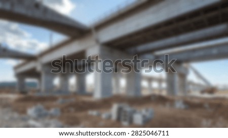 A vast construction site featuring a massive concrete highway overpass supported by numerous pillars under a clear blue sky.