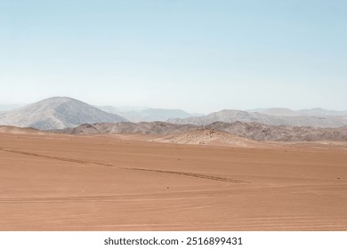 Vast, desolate landscape of the atacama desert, featuring tire tracks cutting across the barren terrain, leading to a distant mountain range under a hazy sky - Powered by Shutterstock