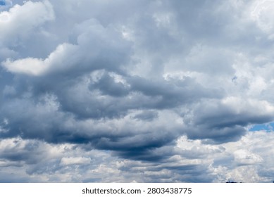 A vast dramatic sky dominated by a dynamic interplay of dark heavy grey clouds and bright white cumulus formations. Glimpses of clear blue sky peek through suggesting transitional or unsettled weather.