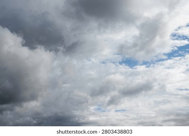 A vast dramatic sky dominated by a dynamic interplay of dark heavy grey clouds and bright white cumulus formations. Glimpses of clear blue sky peek through suggesting transitional or unsettled weather.