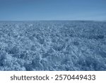 A vast field of jagged ice ridges and densely packed glacial ice stretches endlessly across the surface of the Eqip Sermia Glacier in Greenland under a clear blue sky