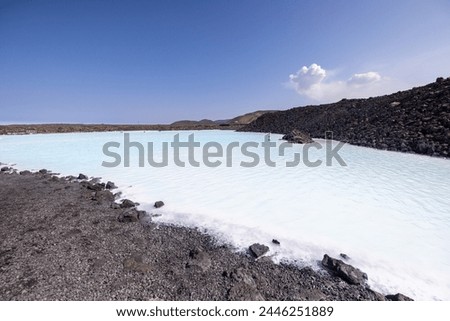 A vast lake nestled among rocky slopes, under a clear blue sky with fluffy clouds. A picturesque natural landscape with a serene horizon. Blue Lagoon Reykjavik Iceland