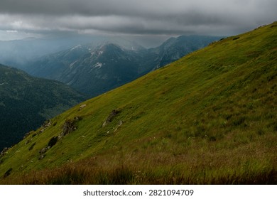 A vast mountain range under a cloudy sky, with lush green slopes leading into distant, misty peaks