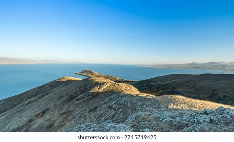 Vast panorama of Lake Sevan in Armenia. Mountains and hills meet the clear blue lake beneath a wide open sky, creating a serene natural landscape.