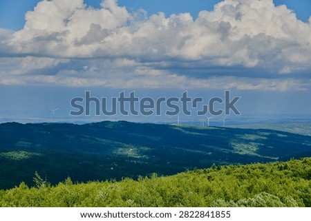 vast panoramic view of rolling green mountain forests and hills in the background, dotted with modern wind turbines along the ridge