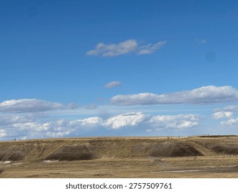 Vast prairie landscape with dramatic cloud formations and distant mountain horizon under bright sky