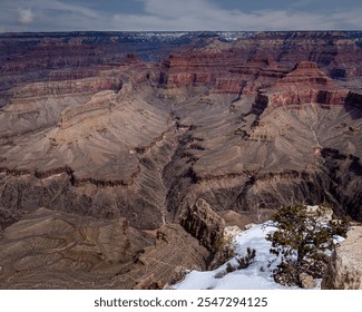 Vast rock formations from the Grand Canyon stretch across the landscape, showcasing an array of deep reds and browns. Snow covers the ground at the rim, adding contrast to the rugged terrain. - Powered by Shutterstock