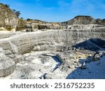 A vast rugged landscape showcasing sunlit stone quarry with layered rock formations on a sunny day. The place is a popular tourist destination called Bukit Jaddih in Madura Island, Indonesia.