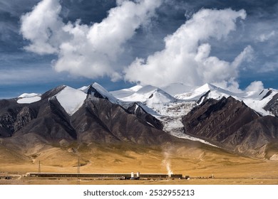 A vast, rugged mountain range with snow-capped peaks, fluffy clouds above, and a steaming train journeying through a serene, grassy landscape. - Powered by Shutterstock