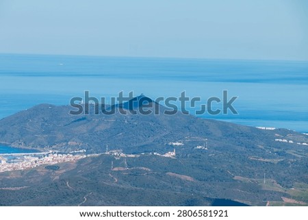 A vast, undulating mountain range in Morocco's Tetouan province meets the calm blue sea under a clear sky, showcasing a serene natural landscape.