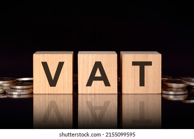 vat - short for Value Added Tax. text on wood cubes with coins, black background, business concept. the inscription on the cubes is reflected from the surface of the black table. front view