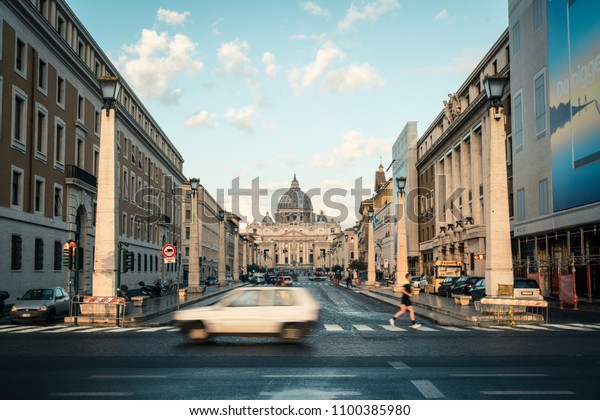 Vatican City, Vatican - Oct 6, 2017: Road traffic\
on the street in front of St. Peter\'s Square and St. Peter\'s Square\
Basilica. It is the famous travel destination of tourist visiting\
Rome, Italy.