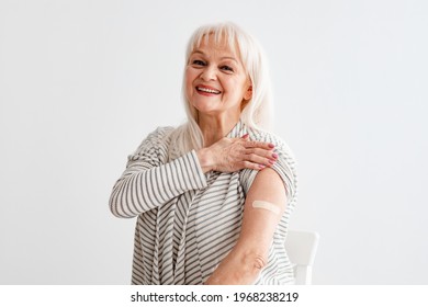 V-Day. Portrait Of Happy Smiling Mature Woman Showing Vaccinated Shoulder With Patch After Antiviral Covid-19 Vaccine Jab, Posing On White Studio Background, Looking At Camera