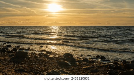 Veczemju Klintis, Latvija, unveils its golden charm as the sun dips below the horizon, casting a radiant glow over the rocky beach during sunset's golden hour. - Powered by Shutterstock