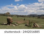 Vedauwoo natural area. Sherman Granite. Medicine Bow-Routt National Park. Large boulders, green grass and bushes under blue sky.  White clouds.  Green meadows and tan rock formations. 