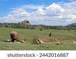 Vedauwoo natural area. Sherman Granite. Medicine Bow-Routt National Park. Large boulders, green grass and bushes under blue sky.  White clouds.  Green meadows and tan rock formations. 