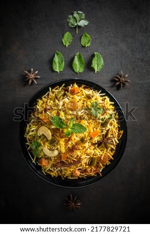 veg biryani tabletop photography styled on black-grey texture background garnished in black a bowl with fresh ingredients like mints leaves, lemon, and star anise. copy space is for the matter.