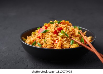 Veg Schezwan Fried Rice in black bowl at dark slate background. Vegetarian Szechuan Rice is indo-chinese cuisine dish with bell peppers, green beans, carrot. Copy space