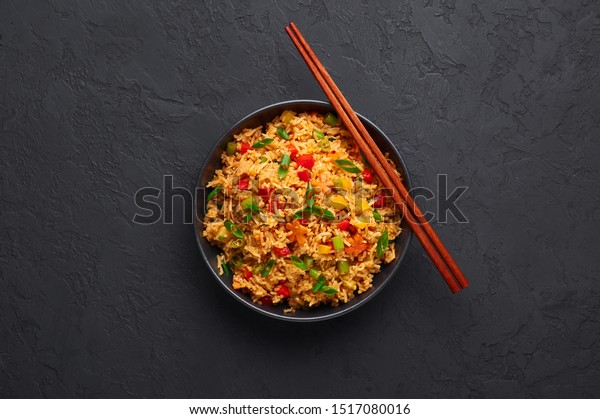 Veg\
Schezwan Fried Rice in black bowl at dark slate background.\
Vegetarian Szechuan Rice is indo-chinese cuisine dish with bell\
peppers, green beans, carrot. Copy space. Top\
view