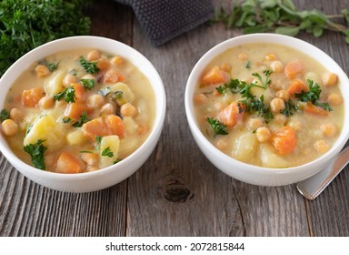 Vegan Chick Pea Soup Or Stew With Potatoes, Root Vegetables And Herbs. Served In 2 Bowls On Wooden Table From Above