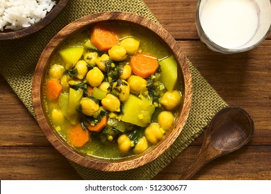 Vegan Chickpea Curry Or Chana Masala With Spinach, Potato And Carrot Served In Wooden Bowl With Lassi Drink, Photographed Overhead With Natural Light (Selective Focus, Focus On The Top Of The Curry)