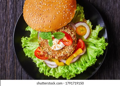 Vegan Chickpea Veggie Burger With Freshly Baked Bun Topped With Sesame Seeds And Lettuce Salad On A Black Plate, Flat Lay, Close-up, Macro