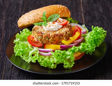 Vegan Chickpea Veggie Burger With Freshly Baked Bun Topped With Sesame Seeds And Lettuce Salad On A Black Plate, Landscape View, Close-up, Macro