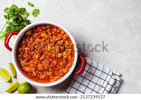 Vegan chili con carne with vegetables and beans in tomato sauce in red saucepan, top view. Mexican food concept.