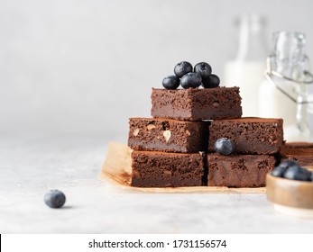 Vegan chocolate brownie with nuts and blueberry. Brownie chewy squares stack with fresh berries and cocoa powder on baking paper. Morning table. Copy space. White background.