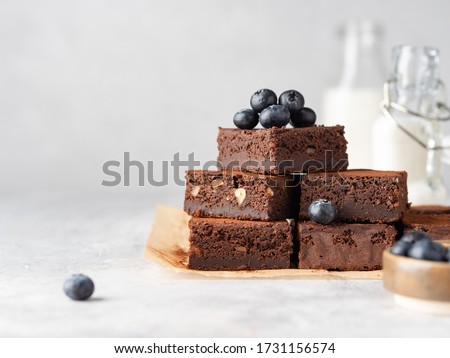 Vegan chocolate brownie with nuts and blueberry. Brownie chewy squares stack with fresh berries and cocoa powder on baking paper. Morning table. Copy space. White background.