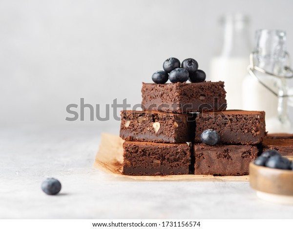 Vegan chocolate\
brownie with nuts and blueberry. Brownie chewy squares stack with\
fresh berries and cocoa powder on baking paper. Morning table. Copy\
space. White background.