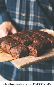 Vegan Chocolate Brownies With Dates And Nuts On Cutting Board. Hands Holding Tray Of Freshly Baked Vegan Vegetarian Chocolate Brownies. Selective Focus