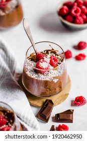 Vegan chocolate mousse desserts in a glass with a spoon, chocolate pieces and fresh raspberries on a light background