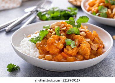 Vegan curry with cauliflower, chickpeas and butternut squash topped with peanuts, served with rice and cilantro
