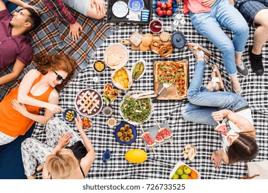 Vegan Food, Holidays, Leisure And People Concept, Top View Of Happy Friends Having Picnic Outdoors Relaxing Lying On Plaid Blanket And Eating