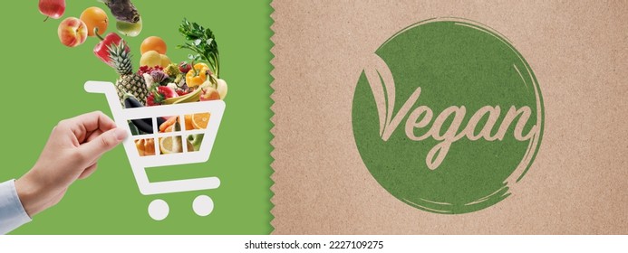 Vegan food online grocery shopping: hand holding a shopping cart icon full of vegetables and fruits - Powered by Shutterstock